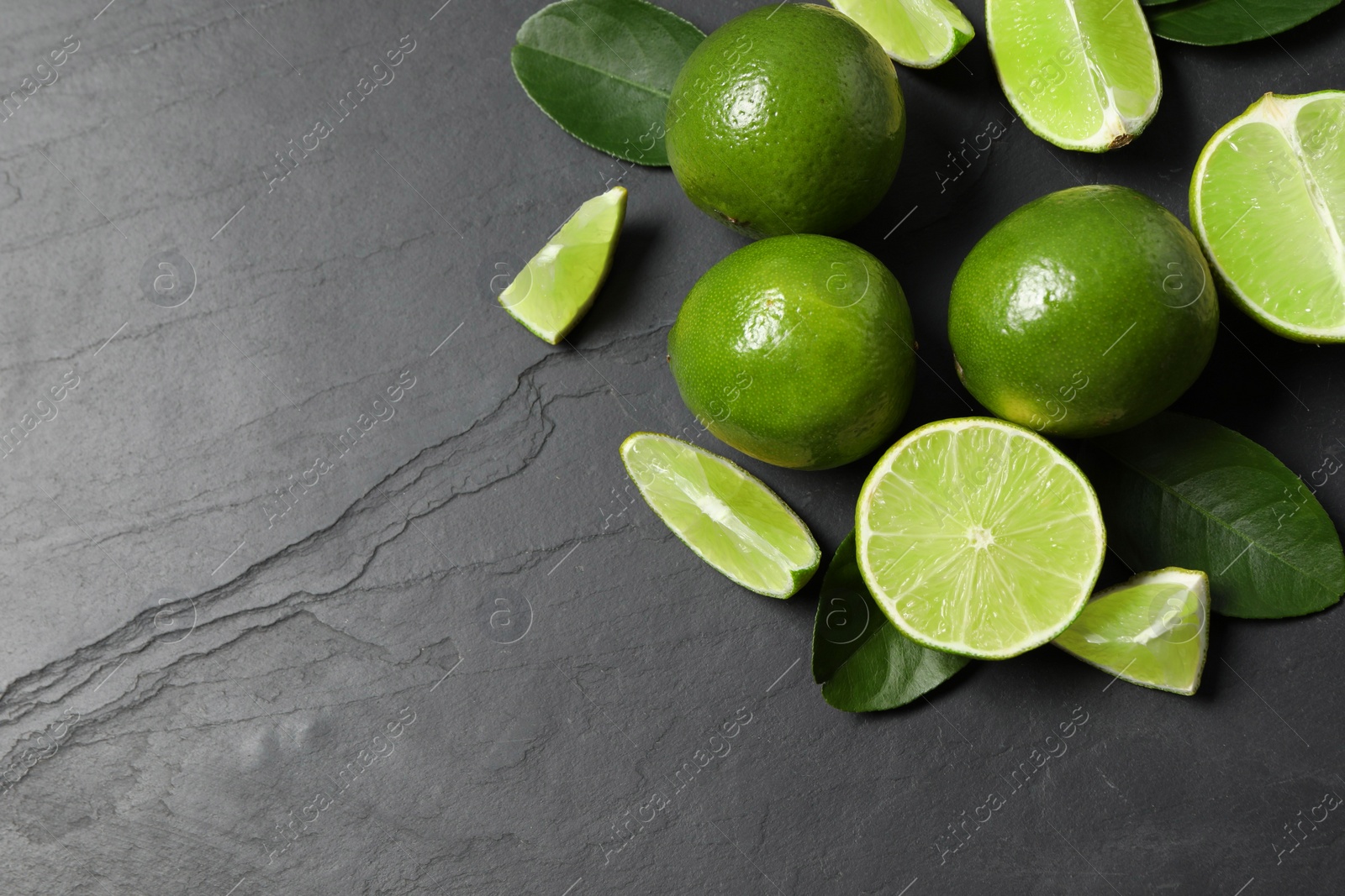 Photo of Fresh ripe limes and leaves on black table, top view. Space for text