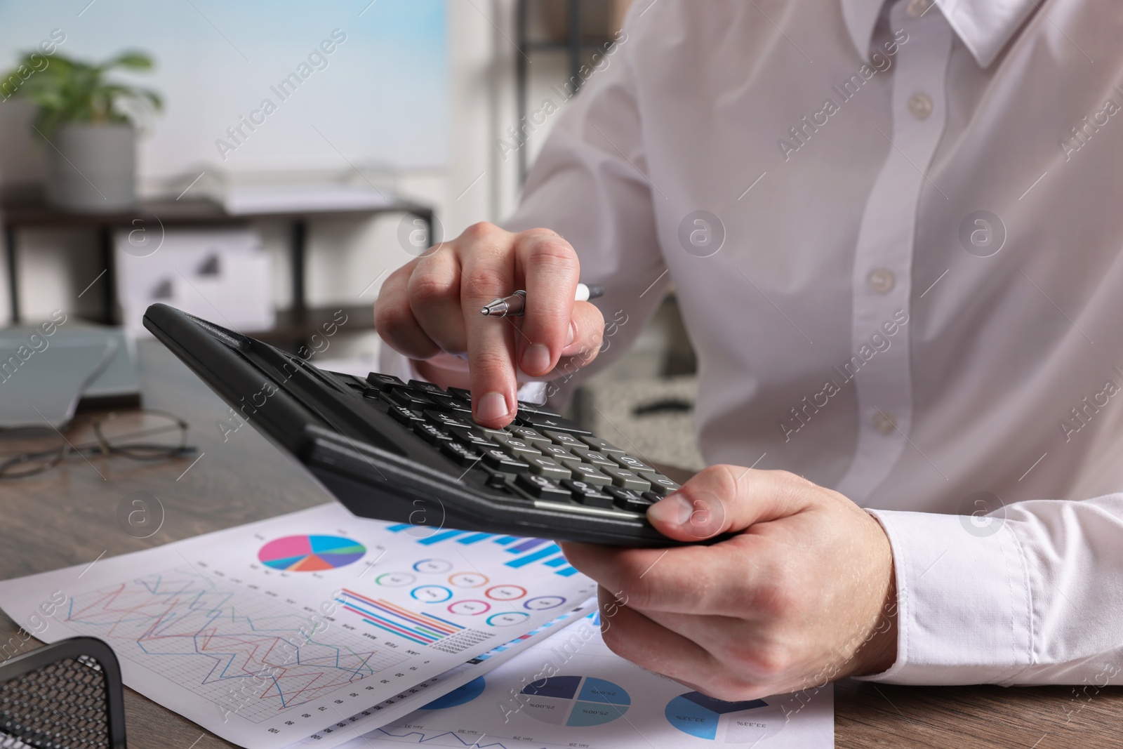 Photo of Man using calculator at wooden table indoors, closeup