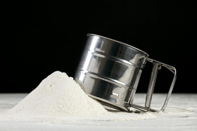 Photo of Sifter and pile of flour on grey table against black background