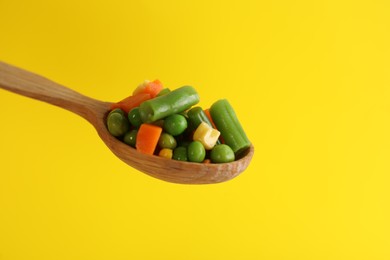 Fresh vegetables in wooden spoon on yellow background, closeup