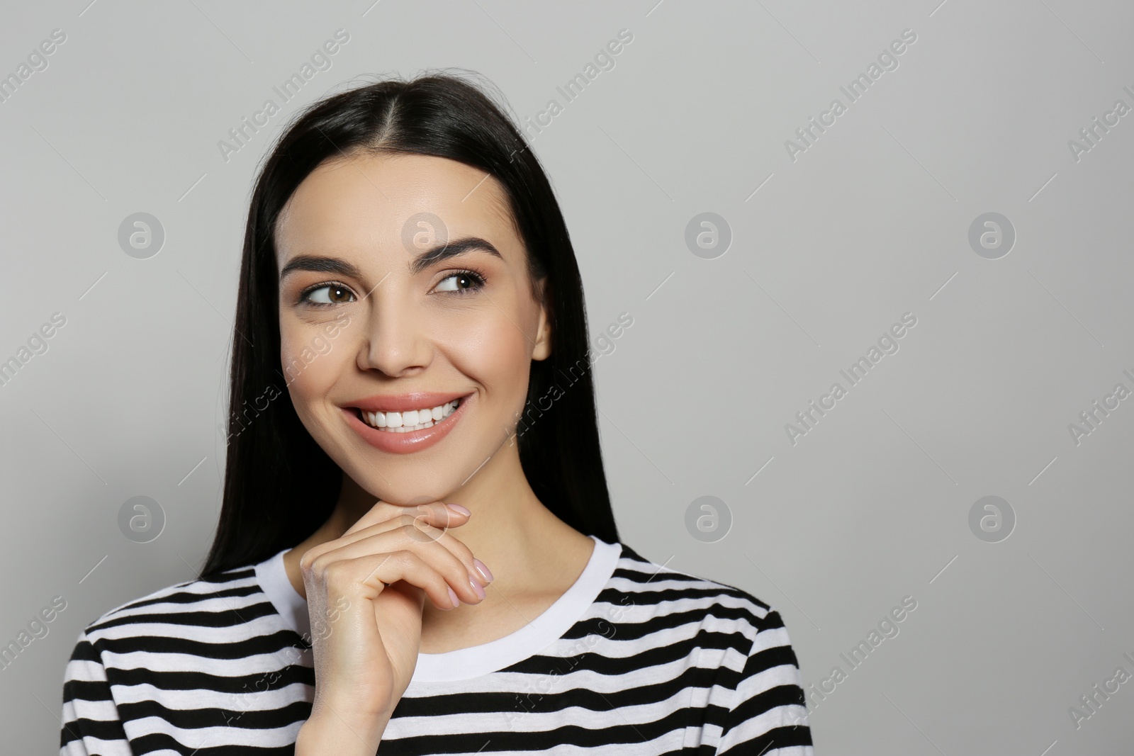 Photo of Portrait of happy young woman with beautiful black hair and charming smile on light grey background, space for text