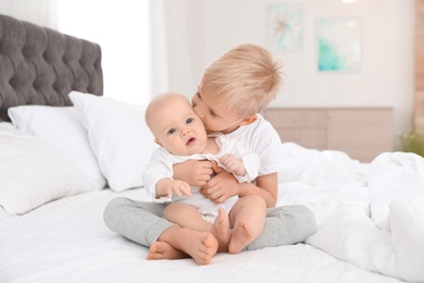 Photo of Cute boy sitting with his little sister on bed at home