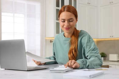 Photo of Woman calculating taxes at table in kitchen