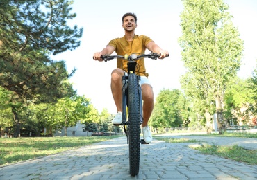 Handsome young man with bicycle in city park, low angle view