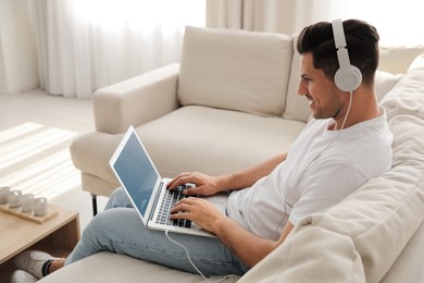 Man with laptop and headphones sitting on sofa at home