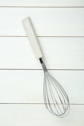 Metal whisk on white wooden table, top view