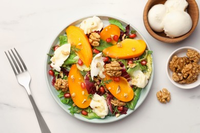 Photo of Delicious persimmon salad with cheese and pomegranate served on white marble table, flat lay