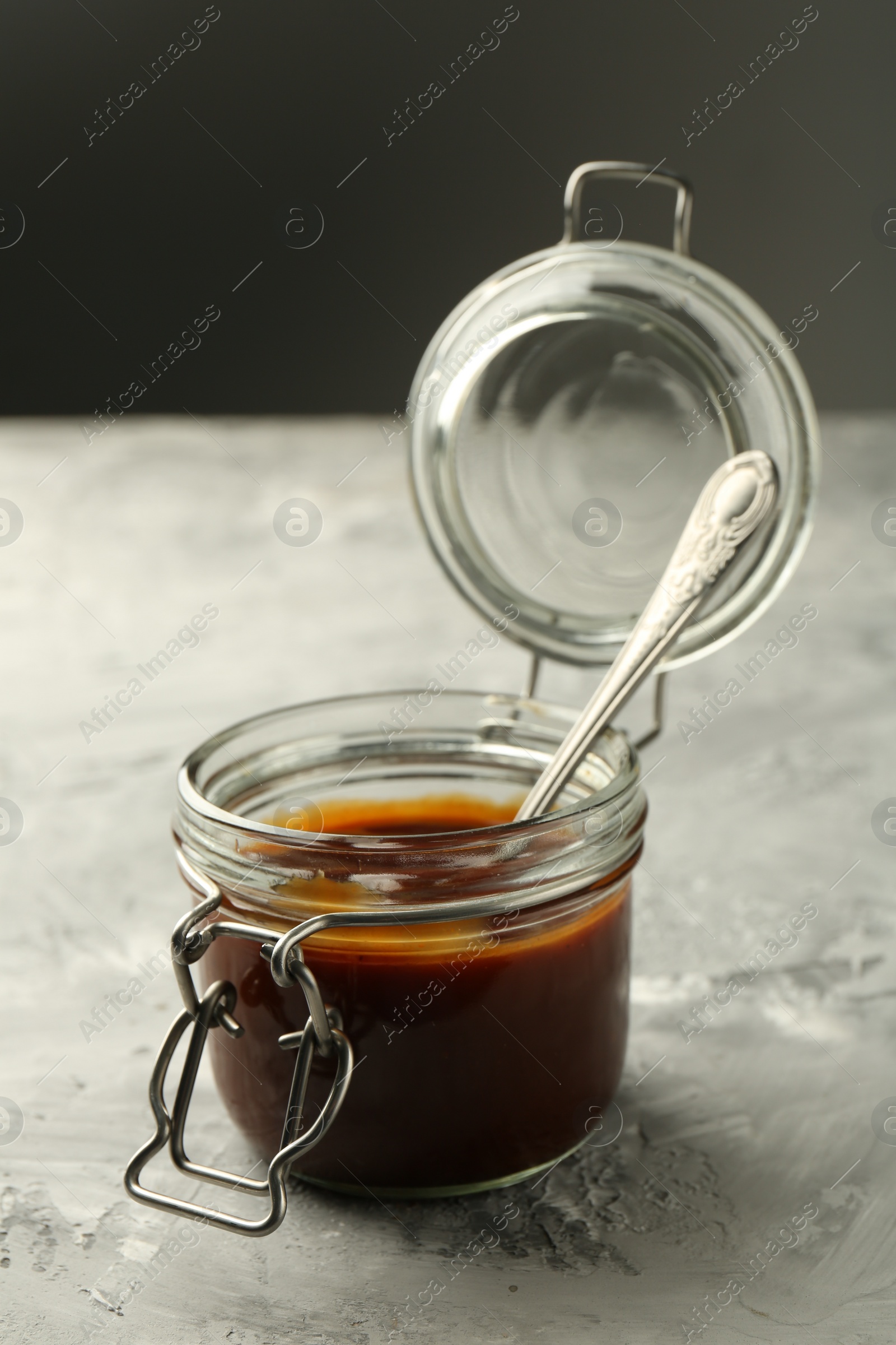 Photo of Tasty barbeque sauce in jar on grey textured table, closeup
