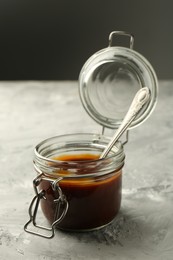 Tasty barbeque sauce in jar on grey textured table, closeup