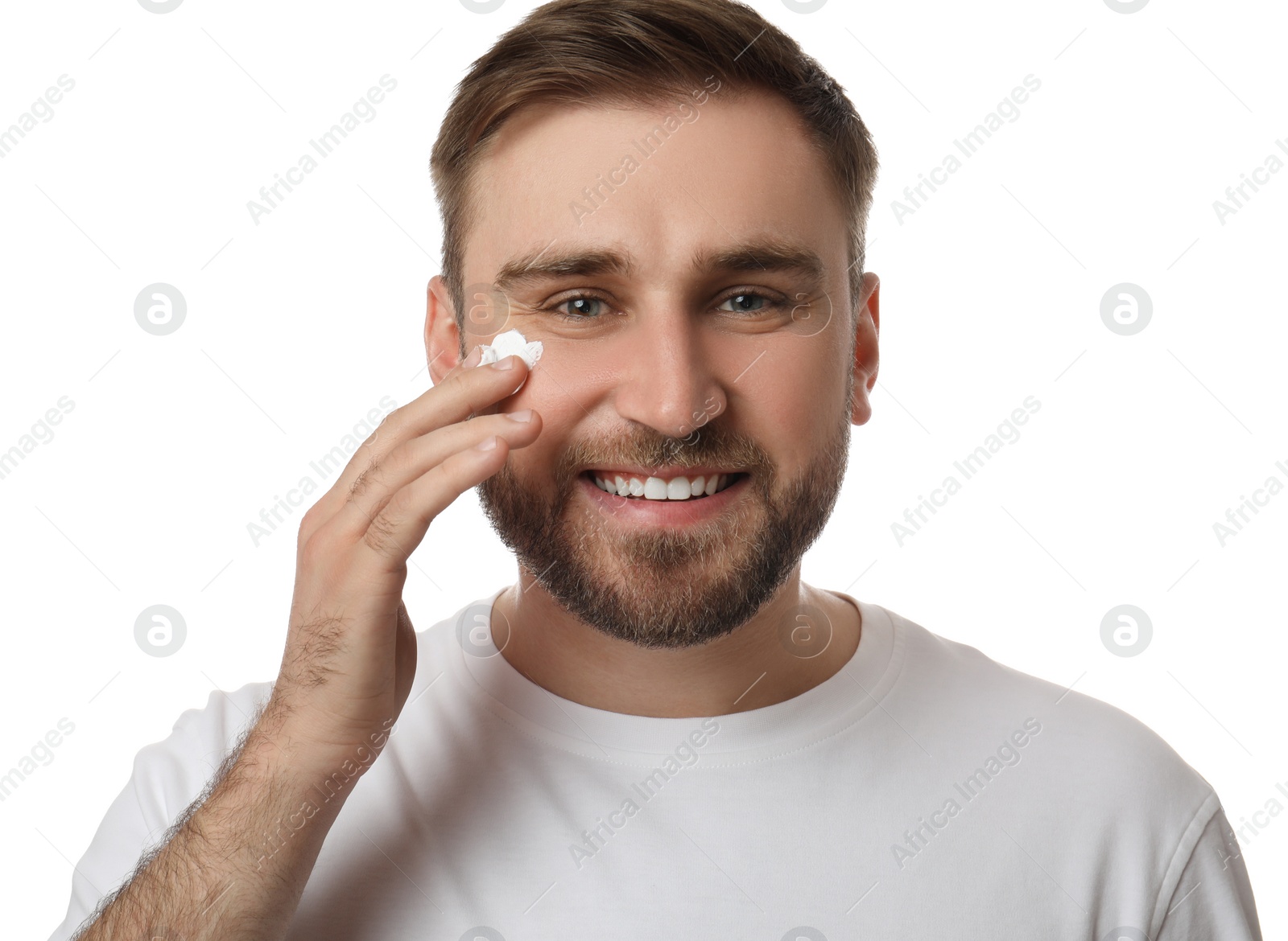 Photo of Happy young man applying facial cream on white background