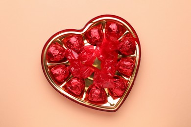 Heart shaped box with delicious chocolate candies on beige background, top view