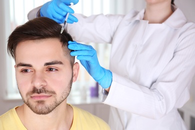 Photo of Young man with hair loss problem receiving injection in salon