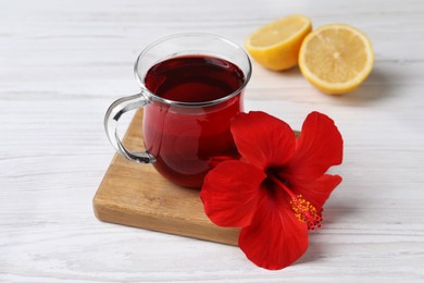 Photo of Delicious hibiscus tea, halves of lemon and beautiful flower on white wooden table