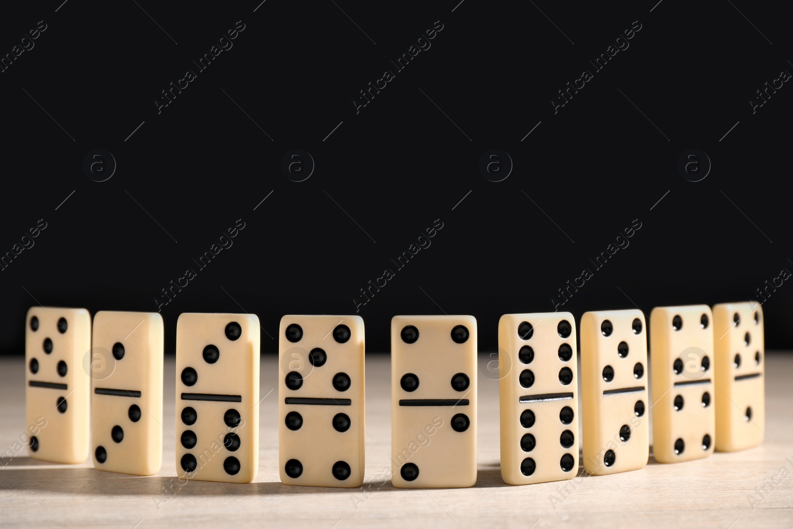 Photo of Domino tiles on wooden table against black background. Space for text