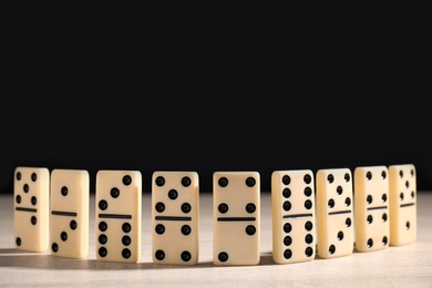 Photo of Domino tiles on wooden table against black background. Space for text