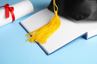 Photo of Graduation hat, open book and student's diploma on light blue background