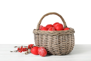 Photo of Wicker basket with painted red Easter eggs on table against white background