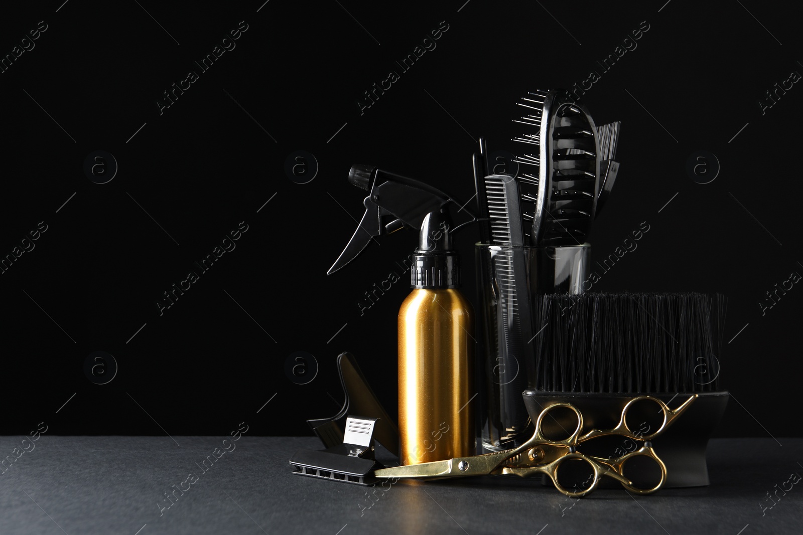 Photo of Different hairdresser tools on grey table against black background
