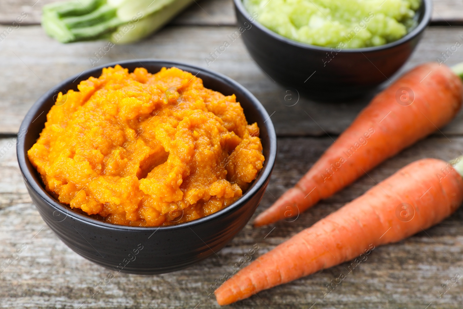 Photo of Tasty puree in bowls, zucchini and carrots on wooden table, closeup