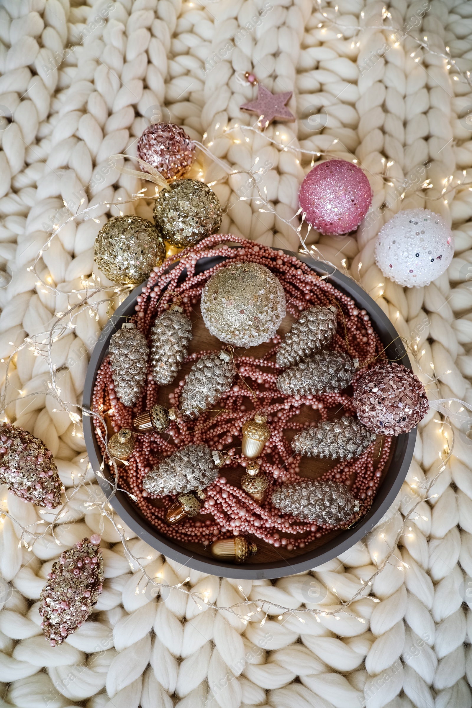 Photo of Beautiful Christmas tree baubles and fairy lights on white knitted fabric, above view