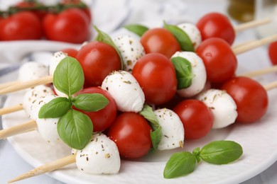 Photo of Caprese skewers with tomatoes, mozzarella balls, basil and spices on plate, closeup