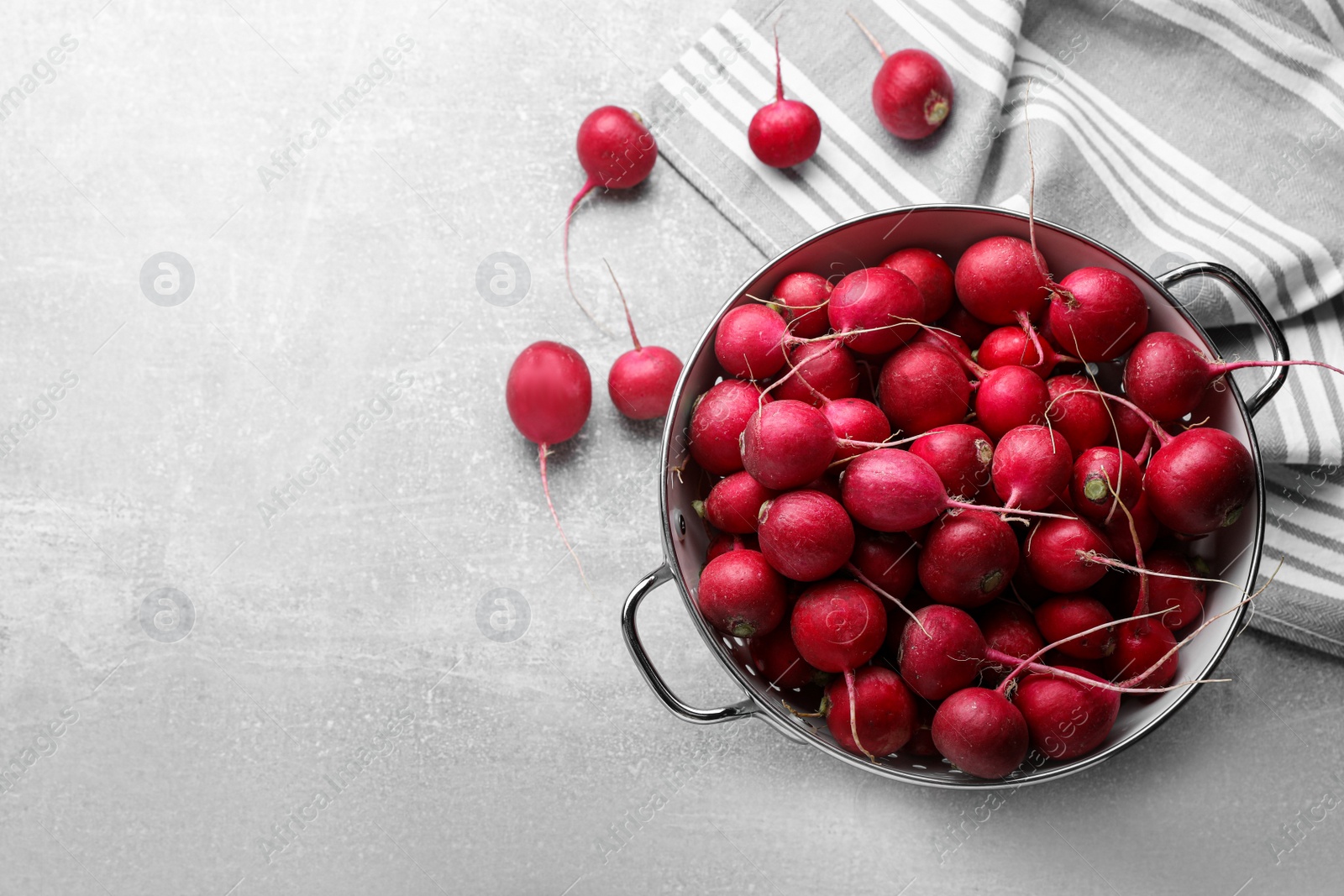 Photo of Colander with fresh ripe radishes on grey table, flat lay. Space for text