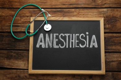 Photo of Blackboard with word Anesthesia and stethoscope on wooden table, top view
