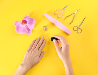 Woman applying nail polish on color background, top view