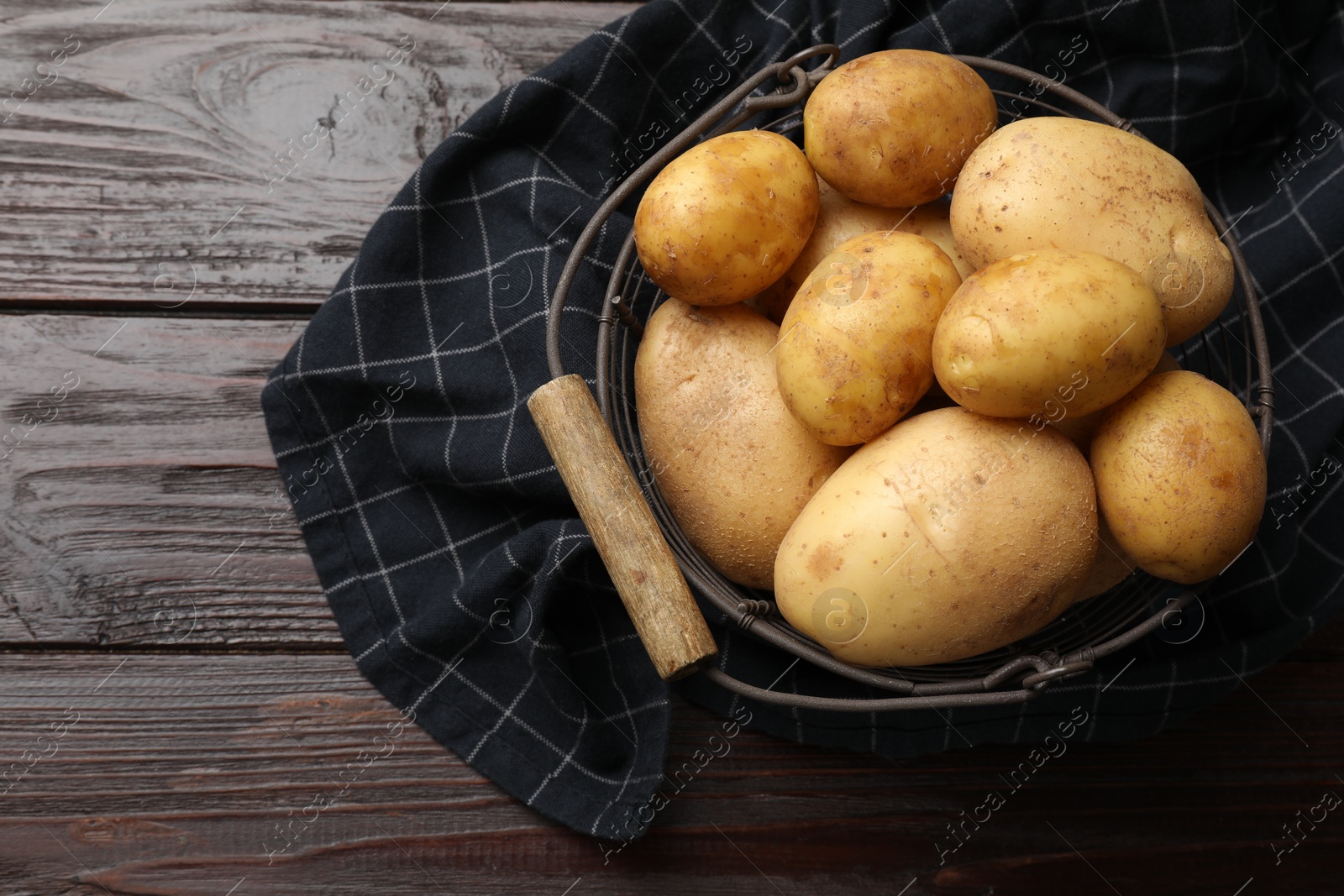 Photo of Raw fresh potatoes in metal basket on wooden table, top view. Space for text