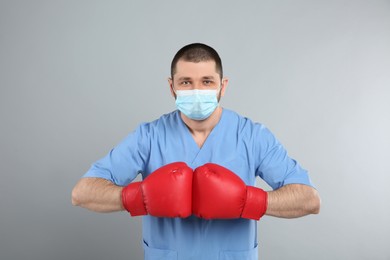 Photo of Doctor with protective mask and boxing gloves on light grey background. Strong immunity concept