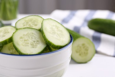 Photo of Cut cucumber in bowl and fresh vegetable on white table, closeup. Space for text