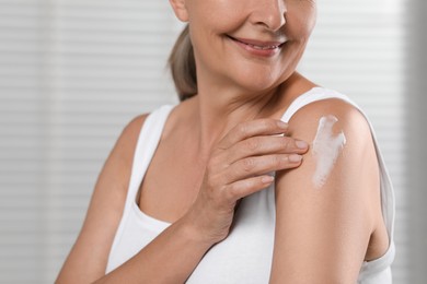 Photo of Happy woman applying body cream onto shoulder on light background, closeup