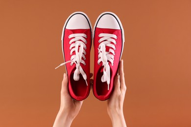 Photo of Woman with red classic old school sneakers on brown background, closeup