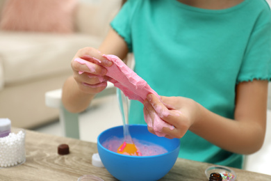 Photo of Little girl making DIY slime toy at table indoors, closeup