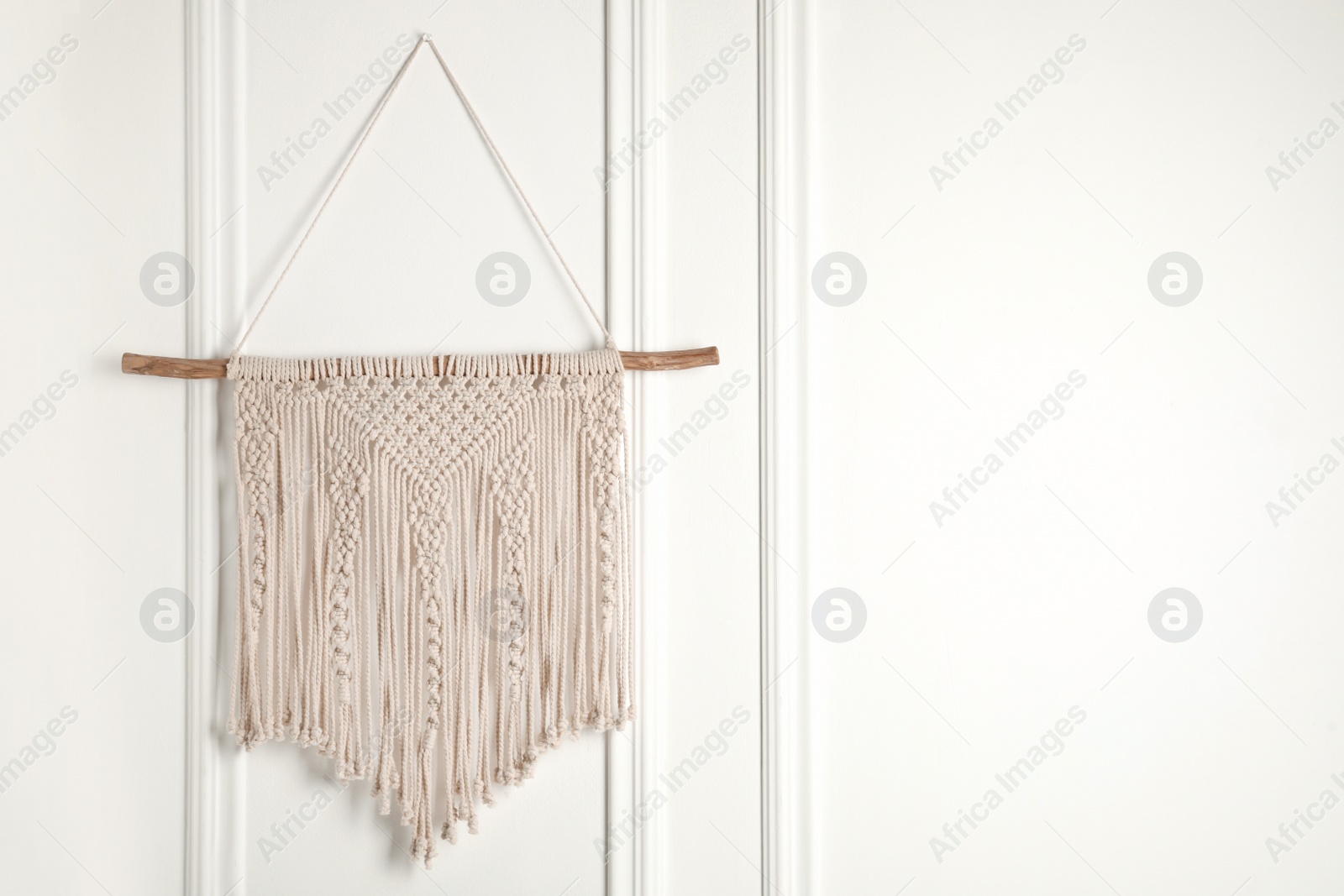 Photo of Stylish beige macrame hanging on white wall. Space for text