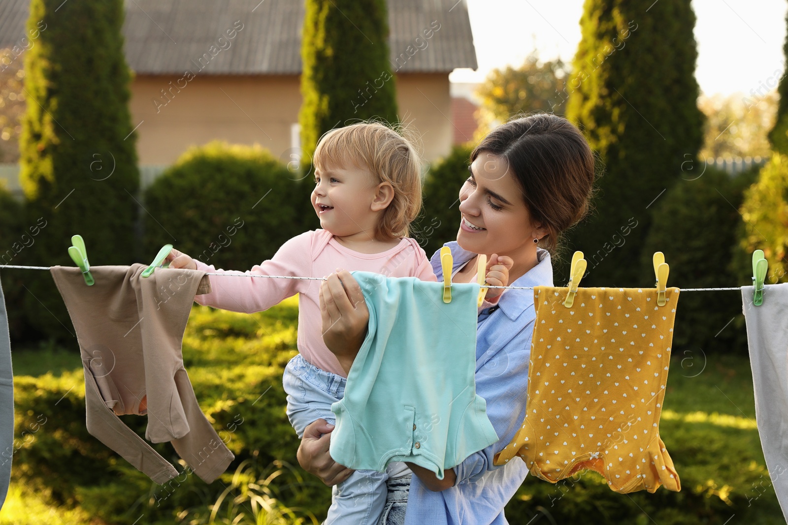 Photo of Mother and daughter hanging clothes with clothespins on washing line for drying in backyard