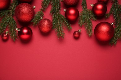Photo of Christmas balls and fir tree branches on red background, flat lay. Space for text