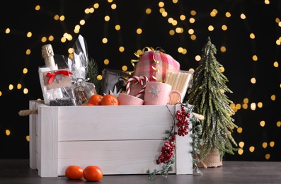 Photo of Wooden crate with Christmas gift set and decor on grey table against festive lights