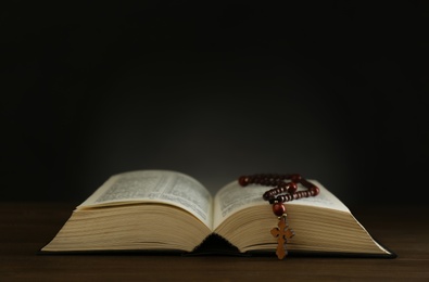 Photo of Open Bible and rosary beads on wooden table, space for text. Lent season