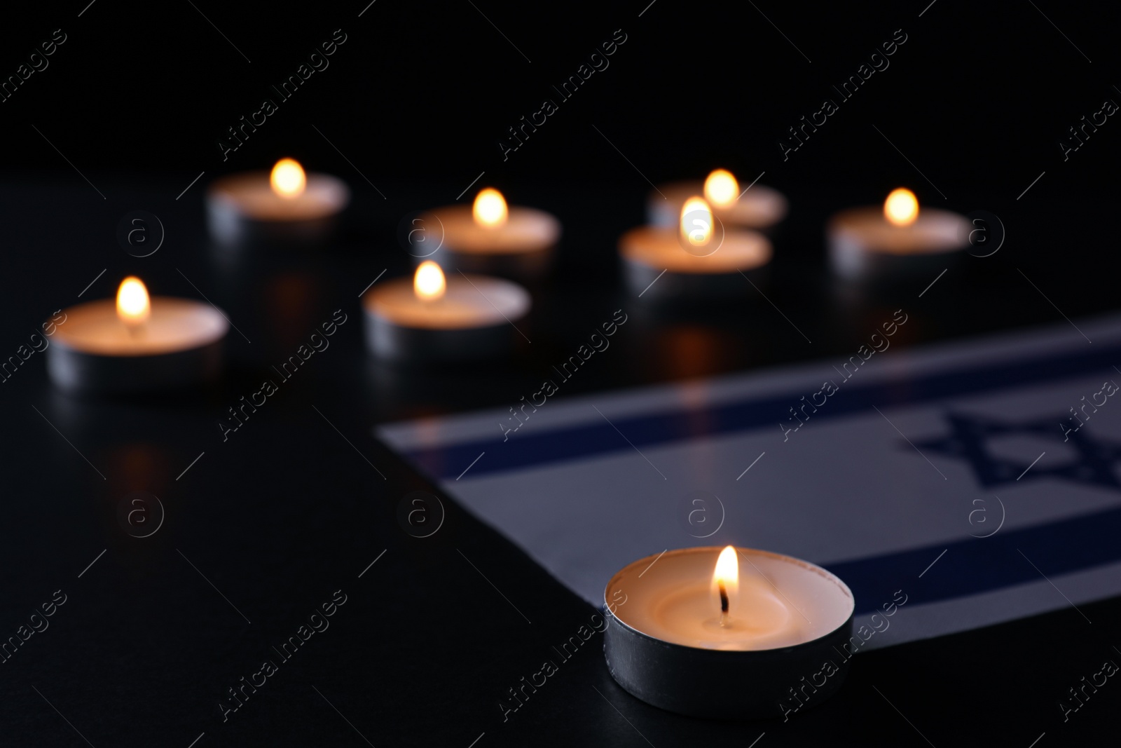 Photo of Burning candle and flag of Israel on black table. Holocaust memory day