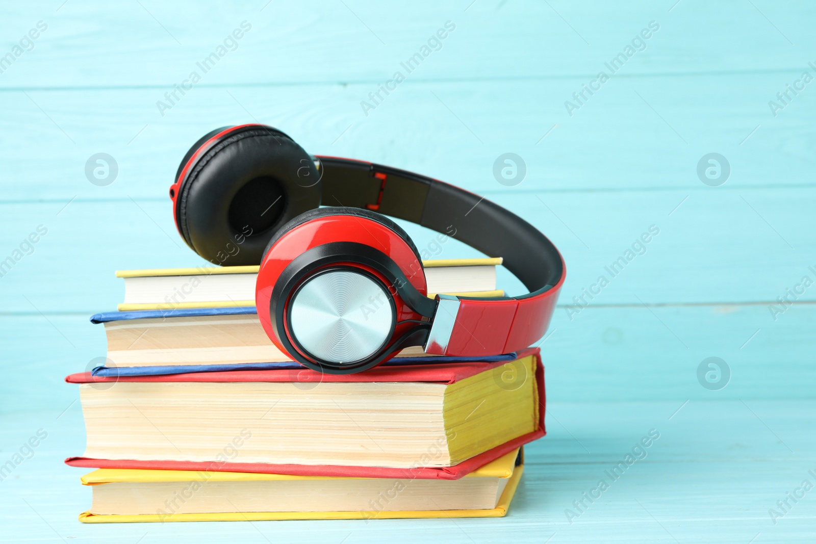 Photo of Books and modern headphones on light blue wooden table