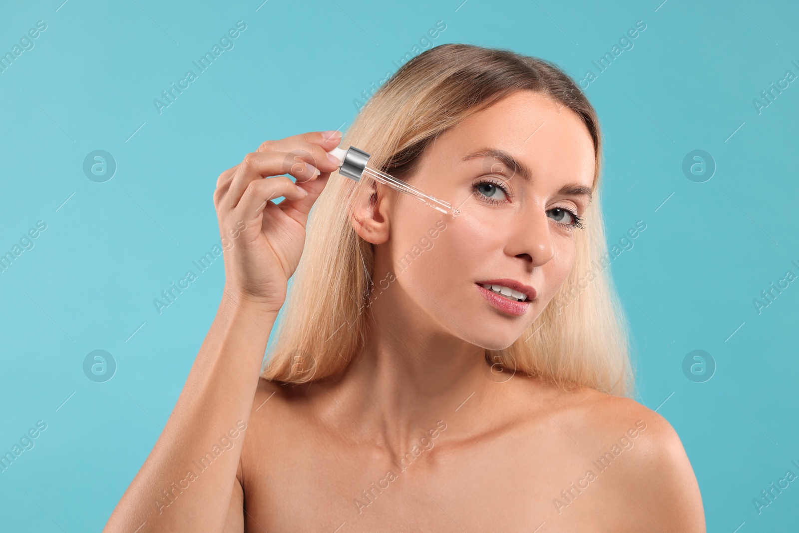 Photo of Beautiful woman applying cosmetic serum onto her face on light blue background