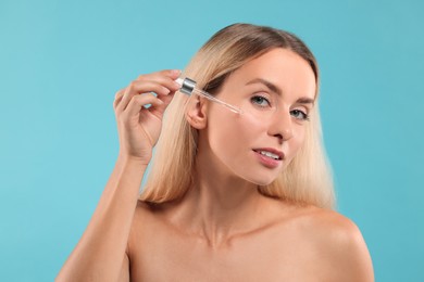 Beautiful woman applying cosmetic serum onto her face on light blue background