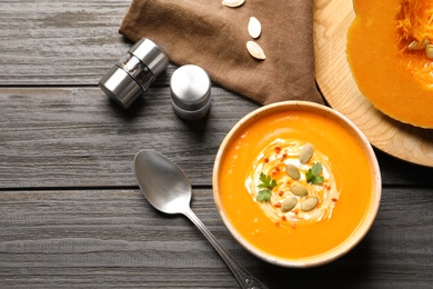 Flat lay composition with bowl of pumpkin soup on wooden background