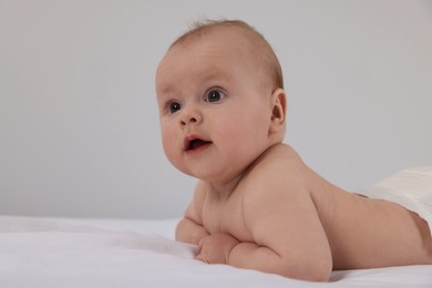 Photo of Cute little baby in diaper lying on bed indoors
