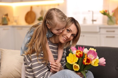 Little daughter congratulating her mom with Mother`s Day at home. Woman holding bouquet of beautiful tulips