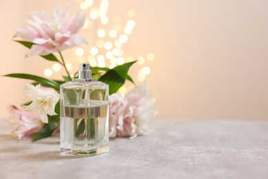 Photo of Bottle of perfume and beautiful lily flowers on table against beige background with blurred lights, space for text