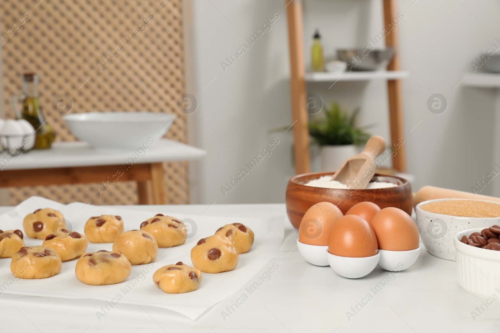 Photo of Fresh dough and different ingredients for cooking chocolate chip cookies on white table in kitchen