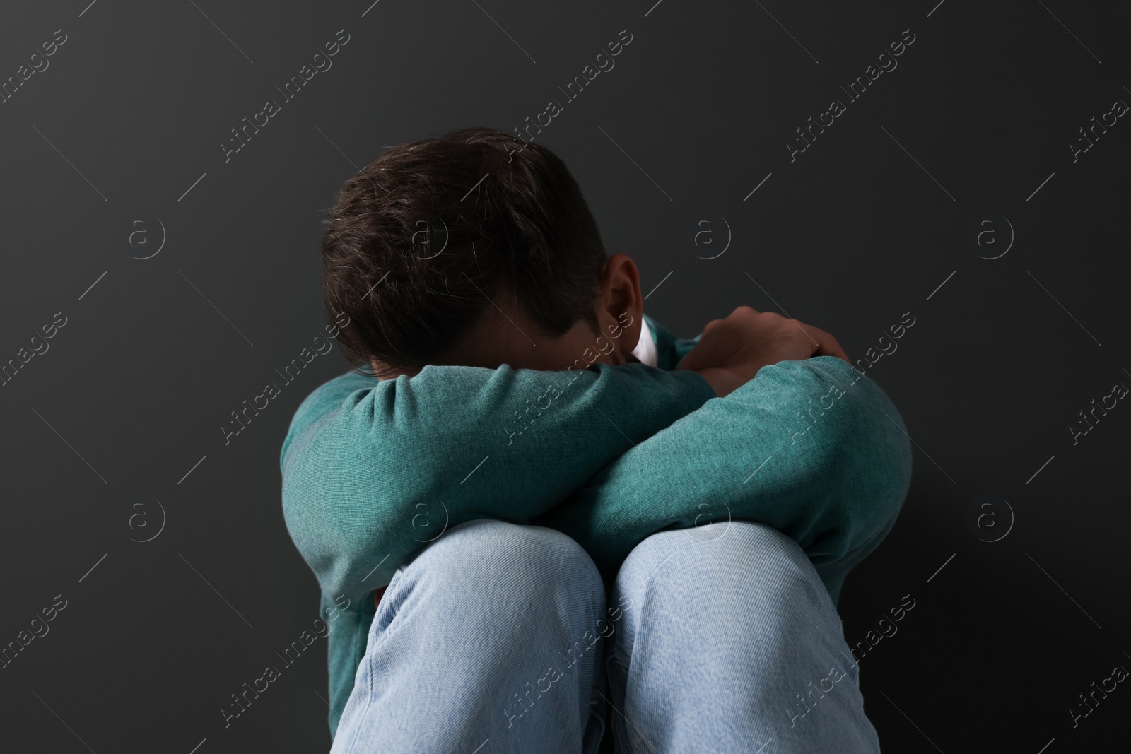 Photo of Upset mature man sitting near black wall