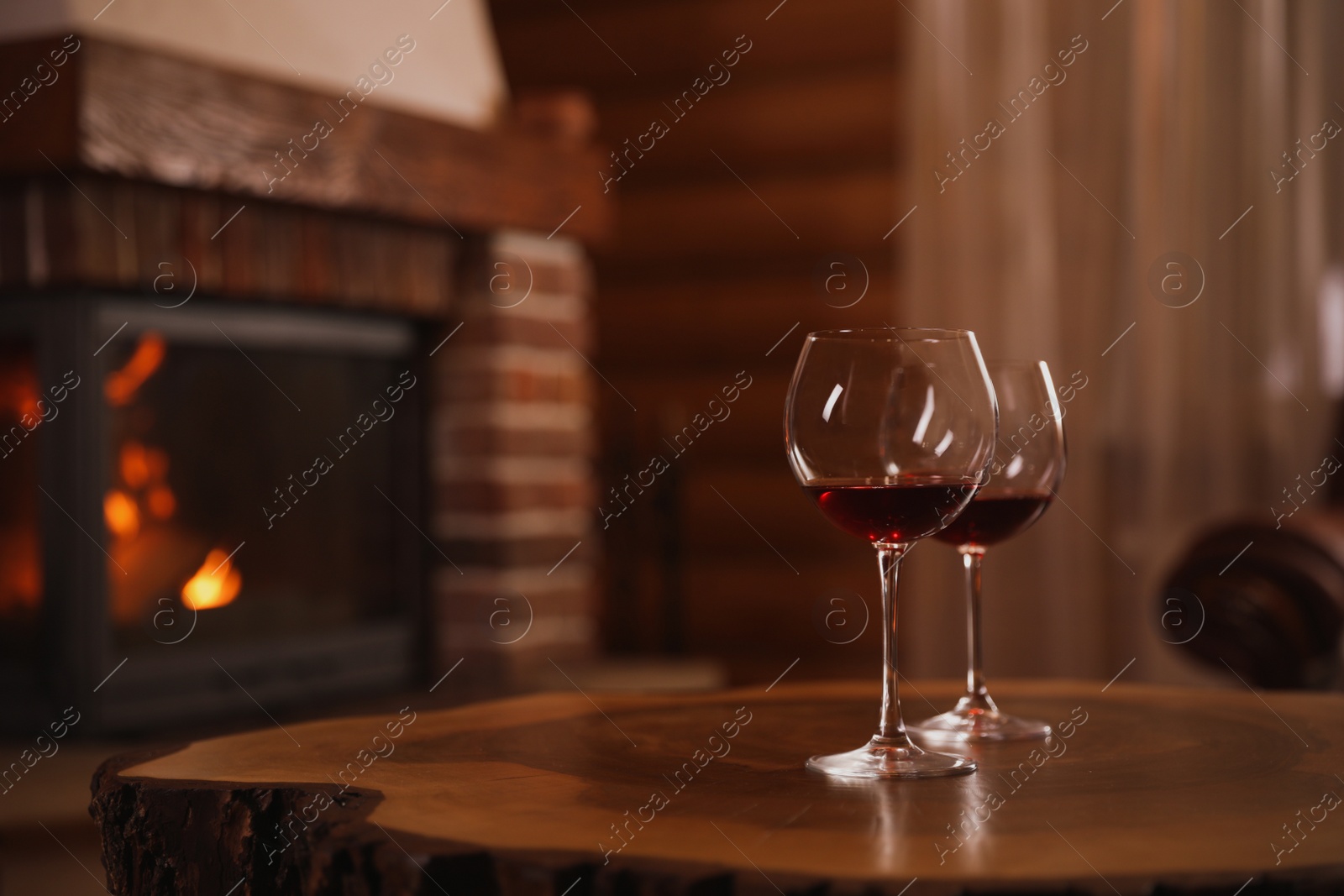 Photo of Glasses of red wine on wooden table near fireplace. Space for text